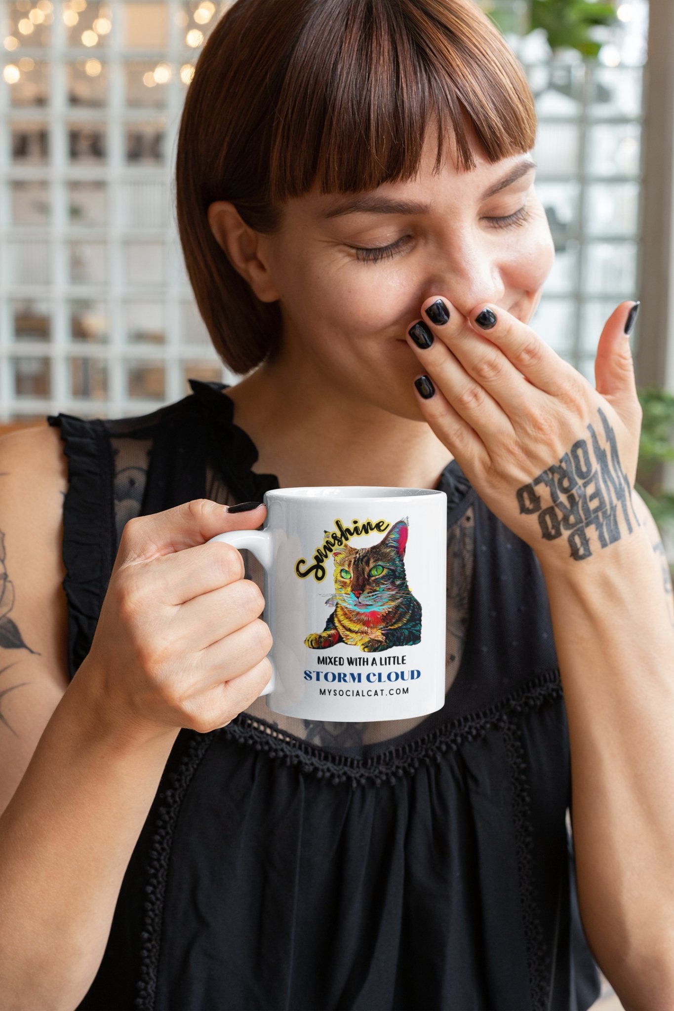 A young woman with short hair smiling and covering her face with her hand, holding a mug