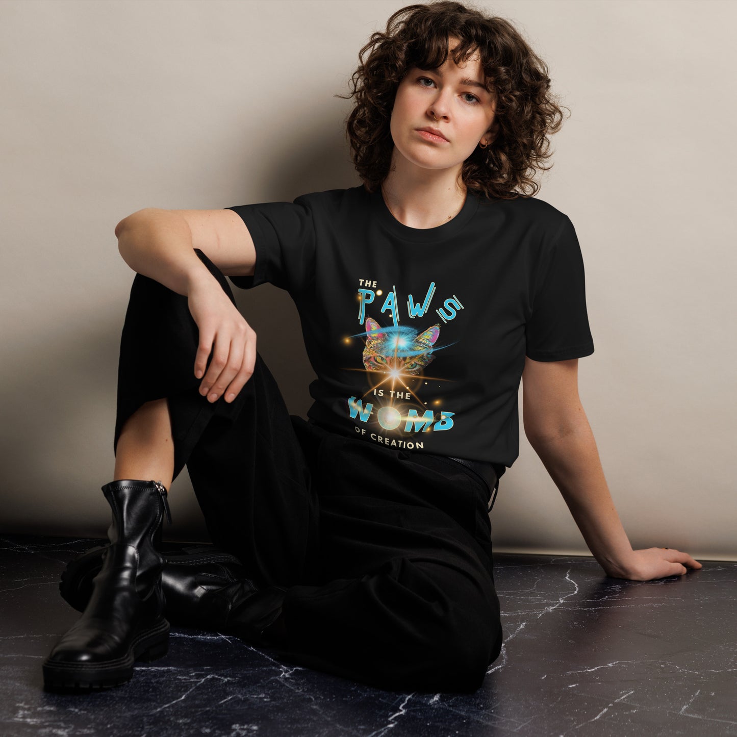 Person wearing a black t-shirt with colorful text design, sitting on a dark surface.