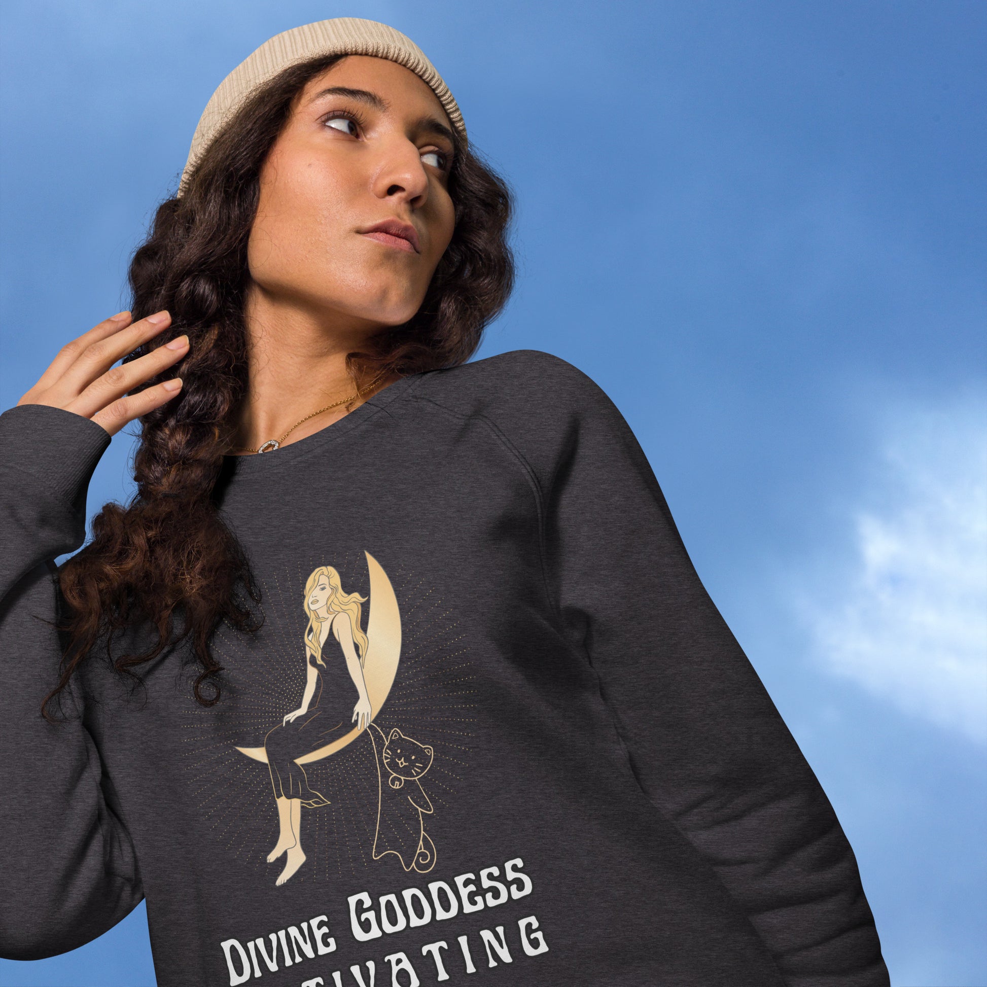 young woman outside blue sky wearing charcoal sweatshirt that says divine goddess activating