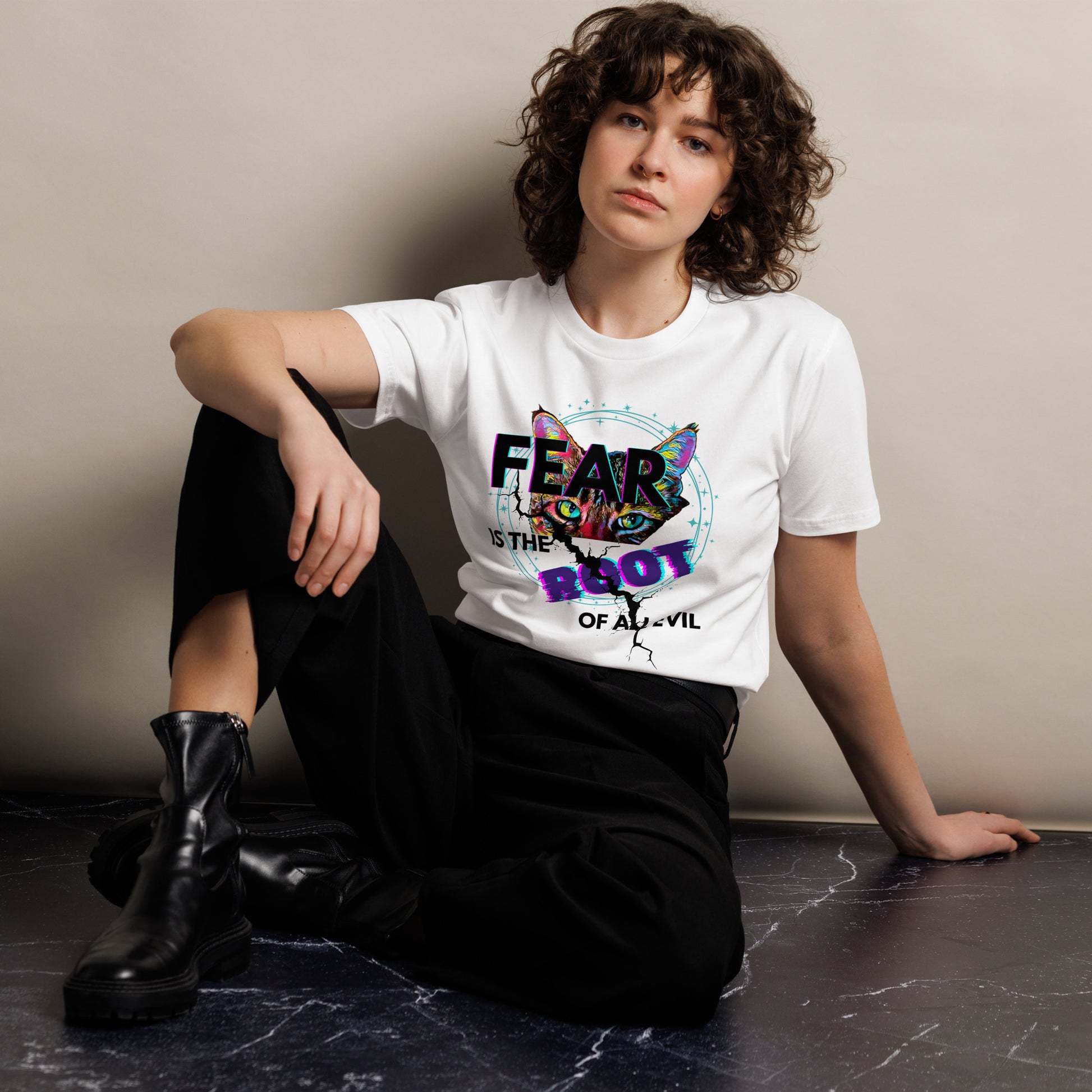 Person wearing a white t-shirt with a colorful graphic and text, sitting on a dark surface.