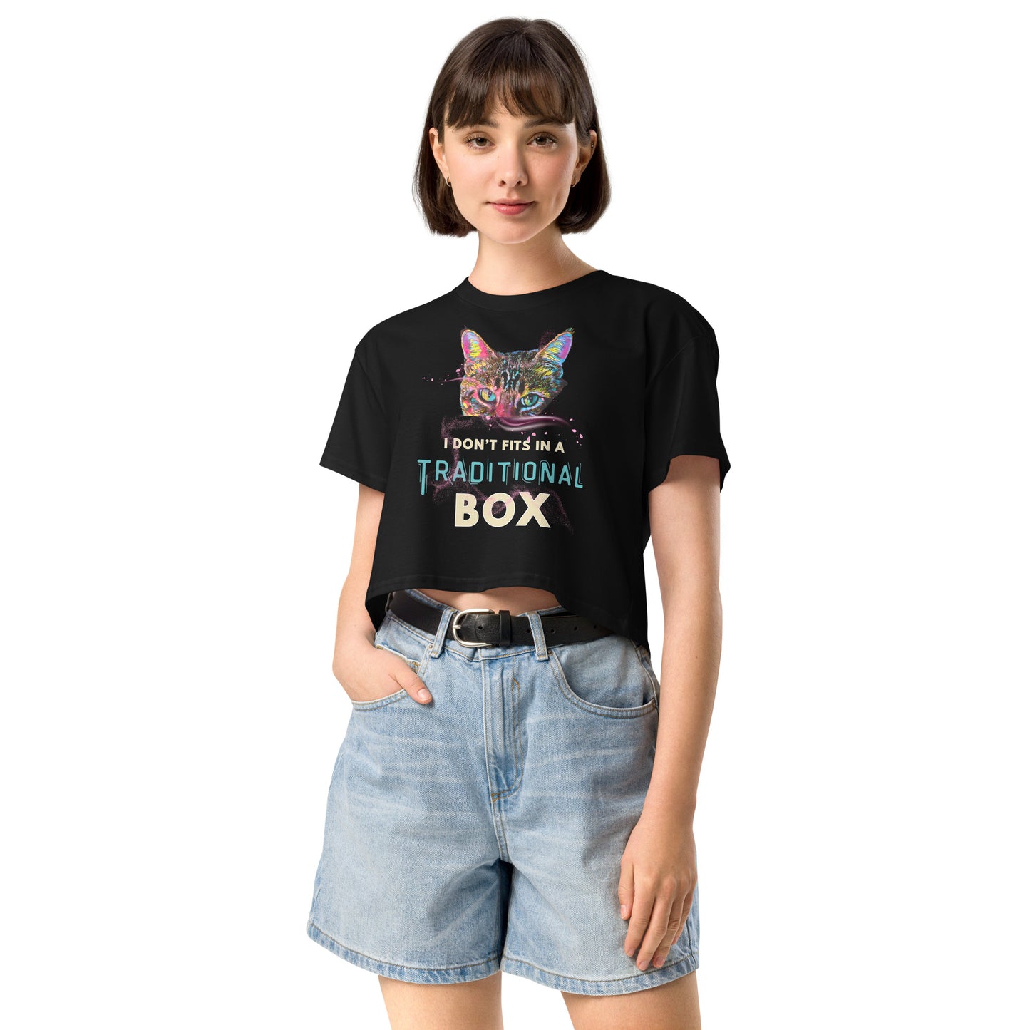 A woman modeling a black graphic t-shirt with a colorful cat illustration and the text 'I DON'T FIT IN A TRADITIONAL BOX', paired with light-wash denim shorts against a plain white background.